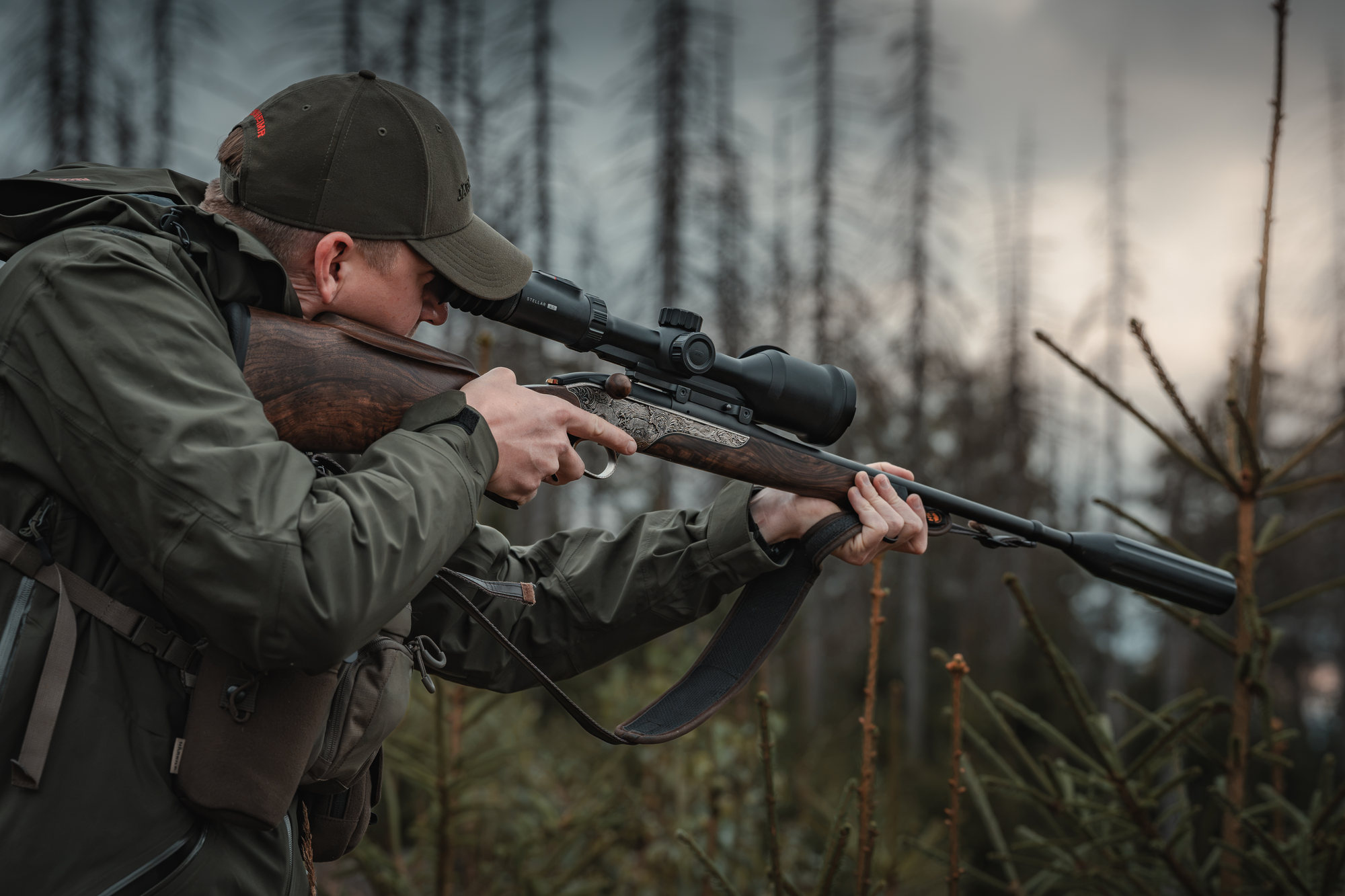 Hunter shouldering a rifle and looking through a Hikmicro Stellar 4.0 thermal scope in the forest