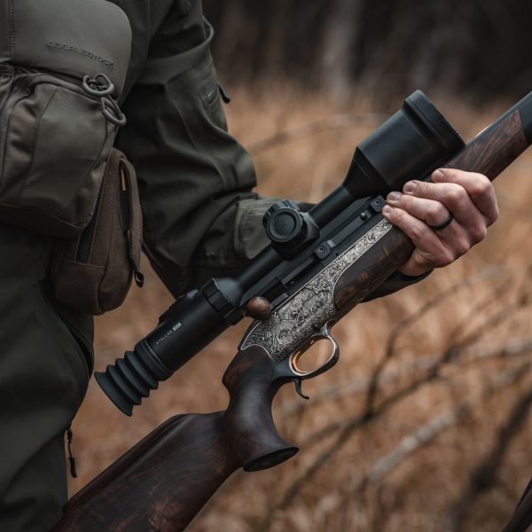 Hunter holding a rifle with a scope fitted, in dry grass