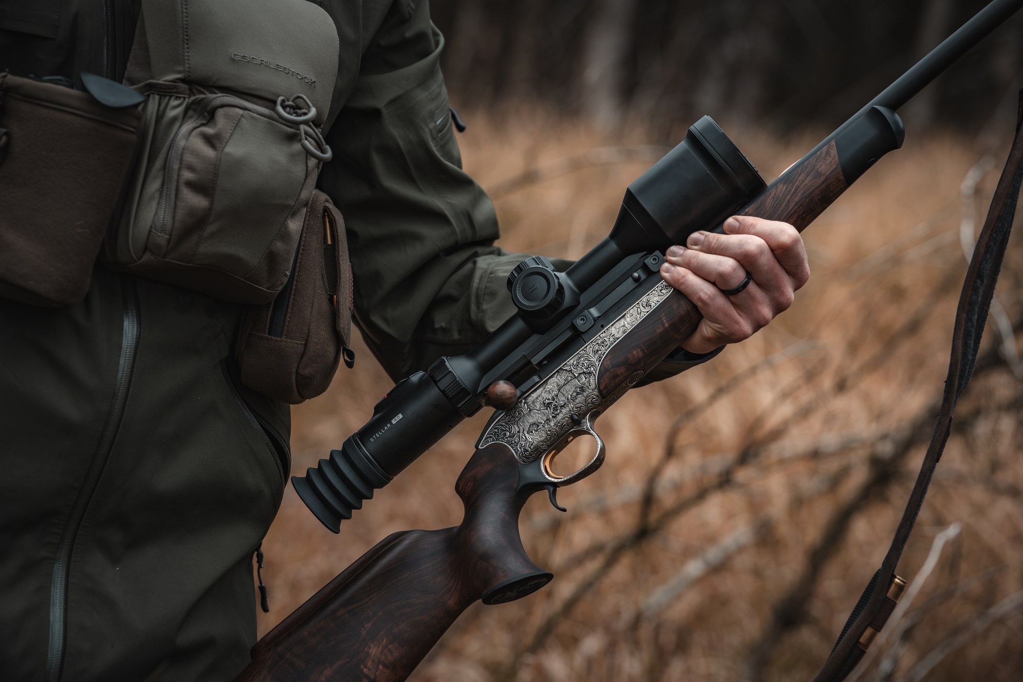 Close-up of a Hikmicro Stellar 4.0 thermal scope fitted to a hunting rifle held in dry grass