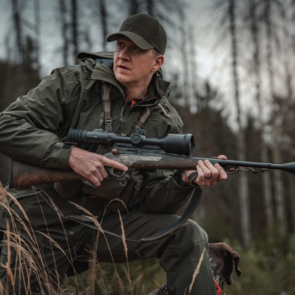 Hunter kneeling in forest with a scoped rifle